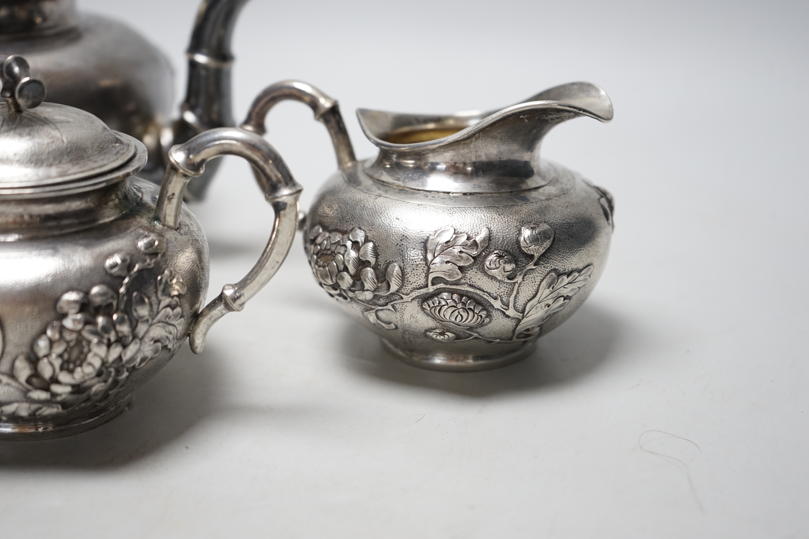 A Chinese white metal three piece tea set, decorated with chrysanthemums, stamped 'Singere', gross weight 32.4oz.